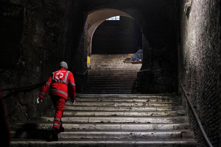 Un trabajador de la Cruz Roja revisa a un indigente durmiendo en una escalinata cerca del Coliseo en Roma, Italia, el 17 de marzo de 2020 (REUTERS/Guglielmo Mangiapane)