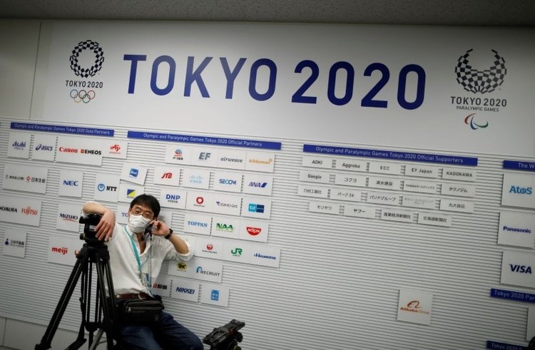 Un camarógrafo con una máscara facial protectora, frente a un cartel que muestra los logos de los Juegos Olímpicos y Paralímpicos de Tokio 2020, en el lugar de conferencia de prensa. 17 de marzo de 2020. REUTERS/Issei Kato