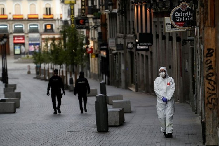 Un trabajador médico con traje protector pasa junto a dos policías en una calle vacía de Madrid, España. 22 marzo 2020. REUTERS/Susana Vera