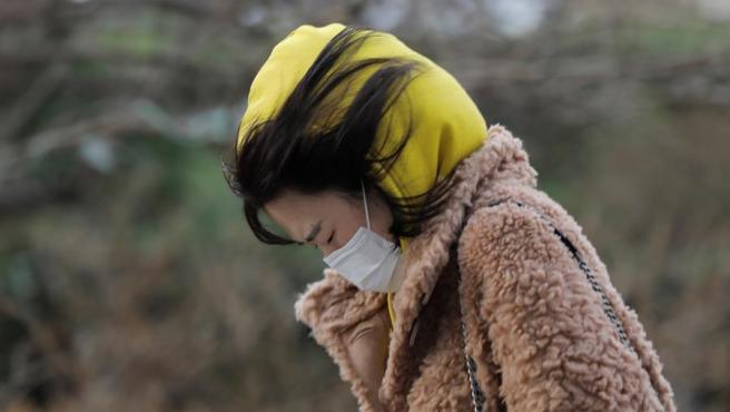 Una mujer con una mascarilla por el coronavirus COVID-19 camina contra el viento en Pekín, China.