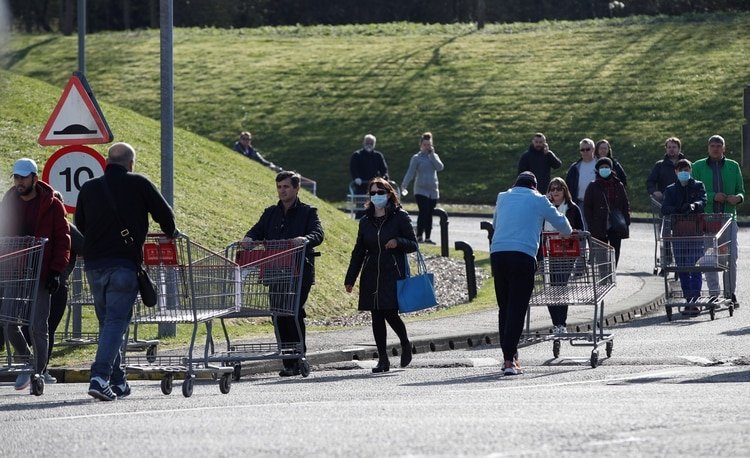Una mujer usa una máscara facial protectora mientras las personas hacen cola fuera del supermercado Costco en Watford (Reuters)