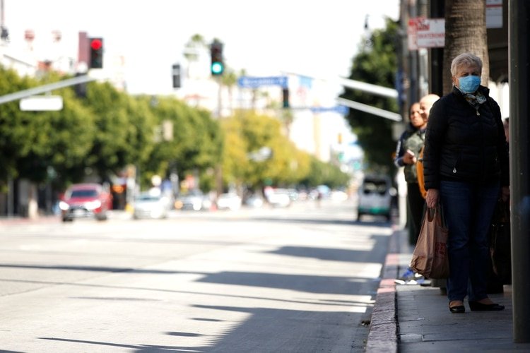 Una persona con una máscara facial espera en la acera durante el brote global de la enfermedad por coronavirus (COVID-19) en Los Ángeles, California, EE. UU., 18 de marzo de 2020. REUTERS / Mario Anzuoni