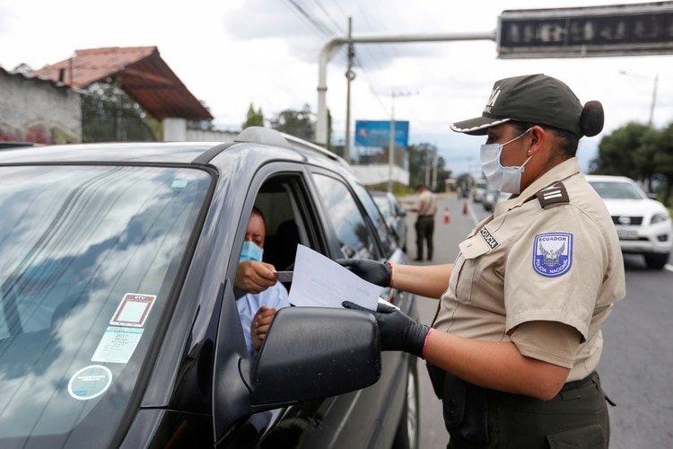 Una oficial de policía ecuatoriana comprueba los documentos de paso seguro de un conductor después de que el gobierno restringiera los viajes dentro del país y declarara un toque de queda nocturno como respuesta a la enfermedad coronavirus