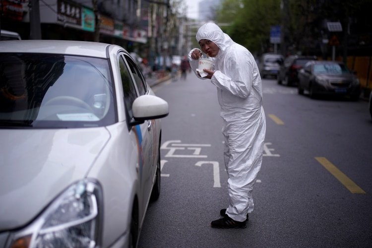 Un hombre come su desayuno vestido con un traje protector en las calles de Wuhan (REUTERS/Aly Song)