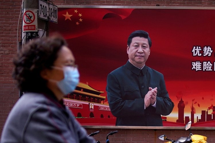 Una mujer con una máscara protectora recorre Shanghái. De fondo, un retrato de Xi Jinping, el responsable del régimen chino que impidió al mundo conocer a tiempo el peligro por el coronavirus (Reuters) 