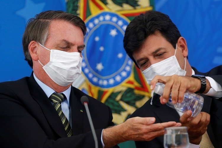 Jair Bolsonaro y el ministro de Salud, Luiz Henrique Mandetta, con máscaras faciales, se higienizan las manos durante una conferencia de prensa el 18 de marzo de 2020. (REUTERS/Adriano Machado)