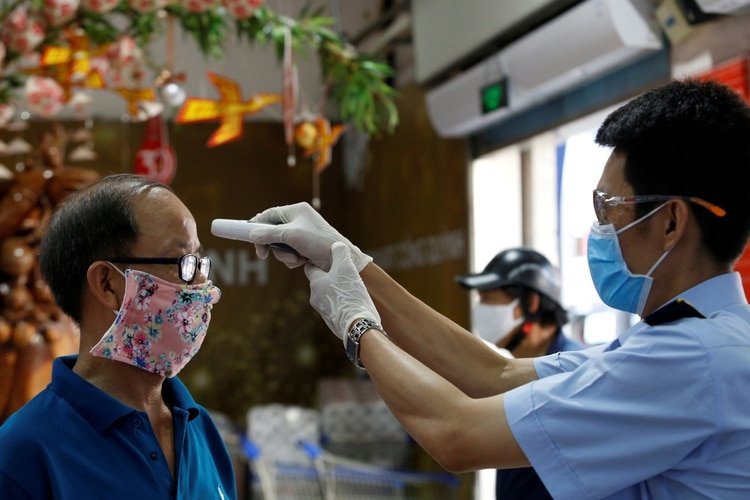 Un hombre le toma la temperatura a un cliente antes de peritirle la entrada a un supermercado