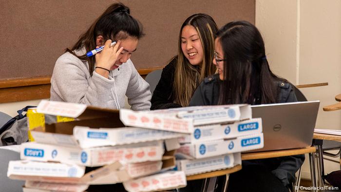 Un grupo de tres estudiantes trabajando tras unas cajas de pizza amontonadas en CruzHacks.