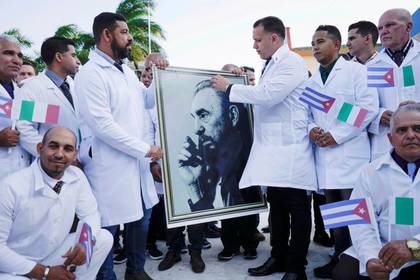 Médicos cubanos sostienen una imagen del fallecido presidente cubano Fidel Castro durante una ceremonia de despedida antes de partir a Italia para ayudar al país europeo, en medio de las preocupaciones sobre la propagación del brote de la enfermedad por coronavirus (COVID-19), en La Habana, Cuba. 21 de marzo de 2020. REUTERS/Alexandre Meneghini.