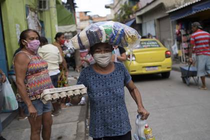 Maria Rita Dias dos Santos, con mascarilla de protección, lleva a su casa comida casera donada por antiguos presos que participan en una organización sin fines de lucro, que da comida a personas que están pasando problemas por la pandemia del nuevo coronavirus, en la favela de Para-Pedro, en Río de Janeiro, Brasil, el viernes 8 de mayo de 2020. (AP Foto/Silvia Izquierdo)